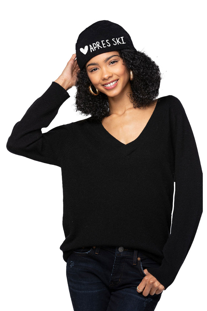 Woman wearing a black cashmere v neck sweater and 'Apres Ski' cashmere black beanie on a white background